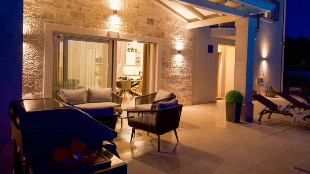 An outdoor patio area with a stone wall, a covered seating area with chairs and a table, and a poolside lounge with sun loungers. - Villa Lavanda Muntrilj with pool (Muntrilj)