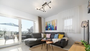 A modern living room with a grey sofa, a coffee table, and a large window overlooking a balcony. - Villa Lavanda Muntrilj with pool (Muntrilj)
