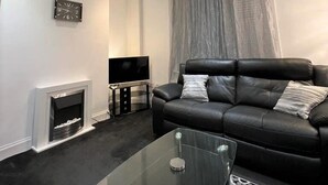 Una sala de estar moderna con un sofá de cuero negro, una mesa de centro de vidrio, un televisor de pantalla plana y una chimenea.