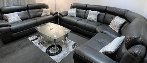 A living room with a sectional sofa, a glass coffee table, and a floor lamp.