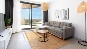 A modern living room with a grey sofa, a round coffee table, and a large window offering a city view. - Marinsa Beach II Sea View/Roof terrace by Interhome (Torrox Costa)