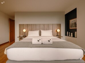 Une chambre d’hôtel moderne avec un grand lit, deux lampes de chevet, une tête de lit en bois et un tableau encadré au mur.