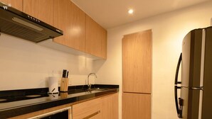 A modern kitchen with wooden cabinets, a black countertop, a stainless steel refrigerator, and a built-in oven.