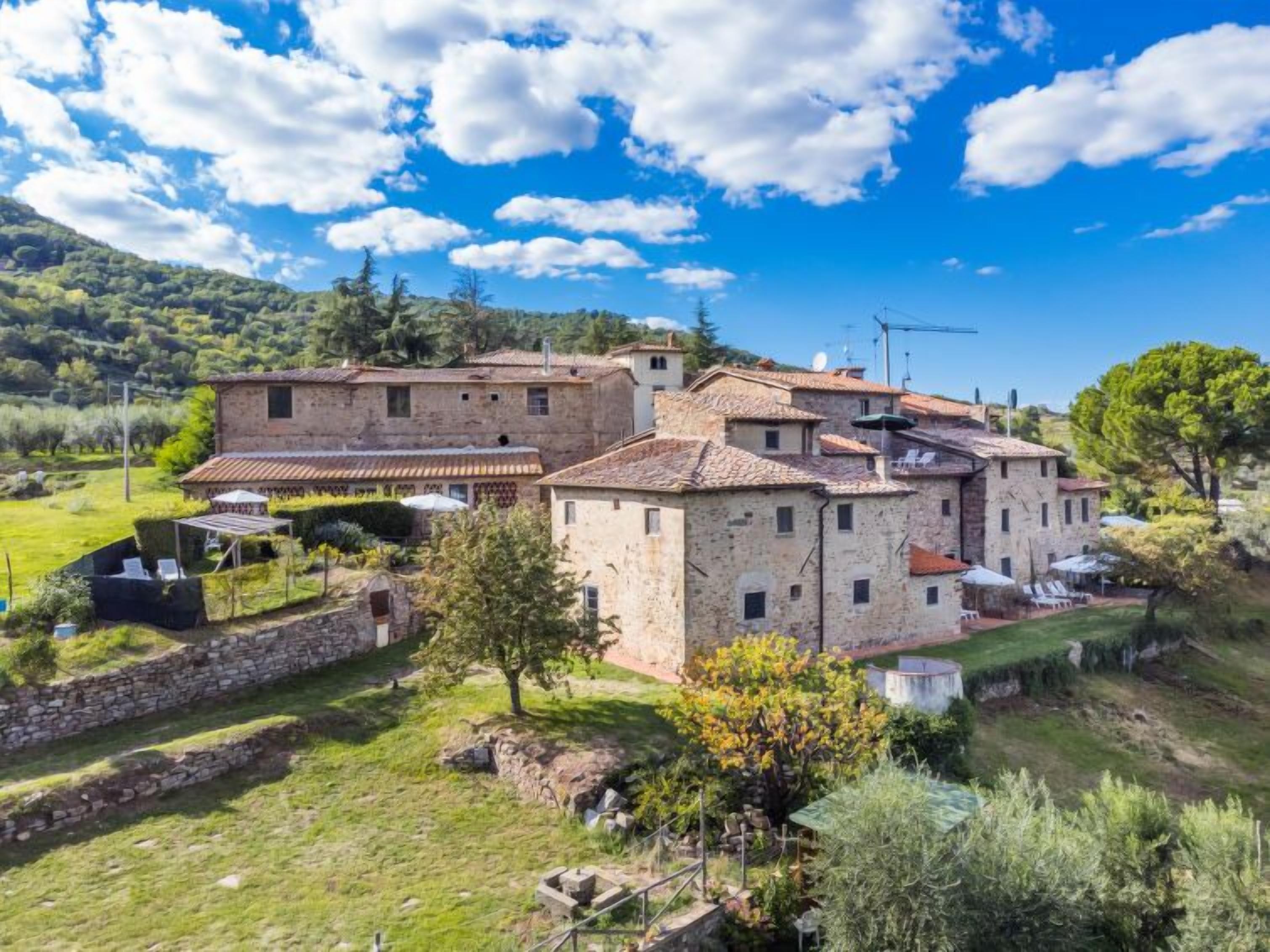 Un edificio in pietra tradizionale con più livelli, circondato da una vegetazione rigogliosa e un cielo azzurro intenso.