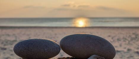 Two smooth stones balanced on a wooden surface with a calm sea and a setting sun in the background.