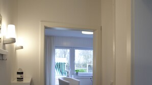 A hallway with a wooden floor leading to a dining area with a white chair and table. - Apartment with private wooden terrace and beach chair (Friedrichskoog)