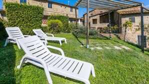 Un cortile con poltrone bianche, una pergola e edifici in pietra.