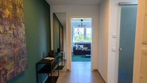 Ein Flur mit einem modernen Kunstwerk links, einer Treppe und Blick in einen Wohnbereich mit Sofa und Tisch.