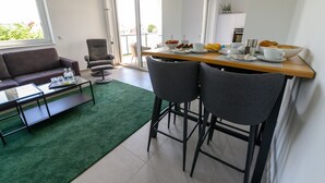 Ein modernes Wohnzimmer mit einem grünen Teppich, einer Couch, einem Couchtisch und einem Essbereich mit einem Holztisch und zwei Barhocker.