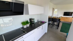 Eine moderne Küche mit weißen Schränken, einer schwarzen Arbeitsplatte, einer Kaffeemaschine und einem Spülbecken. Es gibt einen Essbereich mit Tisch und Stühlen.