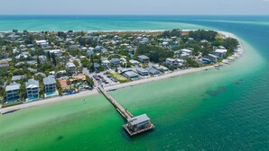An aerial view of a coastal residential area with houses, a pier, and a beach.