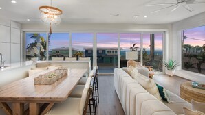 A spacious living area with a wooden dining table, a large sofa, and a view of the ocean through floor-to-ceiling windows.