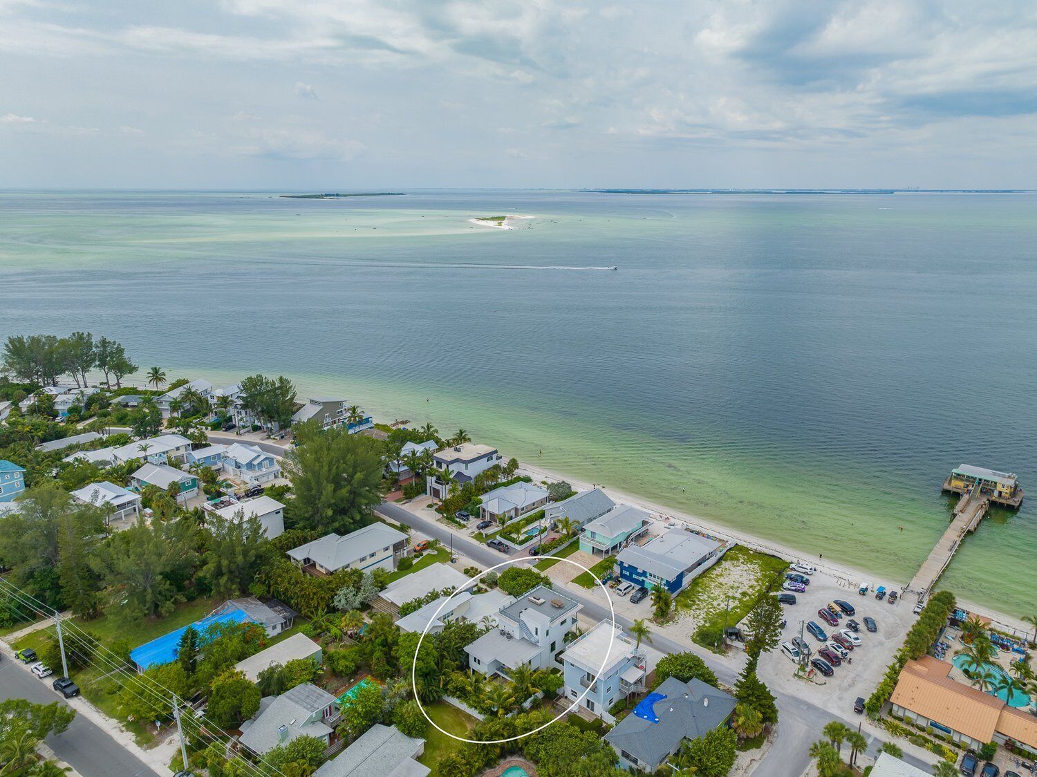 An aerial view of a coastal residential area with houses, a beach, and a pier.