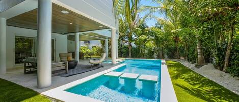 Ett modernt hus med en swimmingpool, utomhusmöbler och frodig grönska.