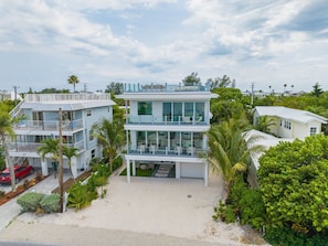 A modern two-story beachfront property with a spacious patio, multiple balconies, and lush greenery.