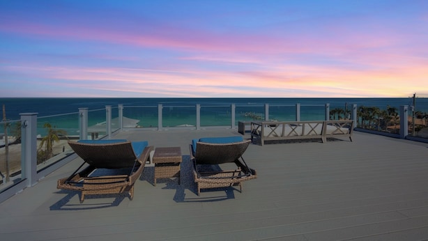 A rooftop terrace with wicker lounge chairs and a table, overlooking a beach and ocean.