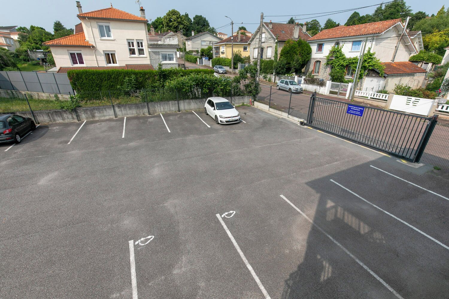 A parking lot with marked spaces, a white car parked, and a gated entrance.