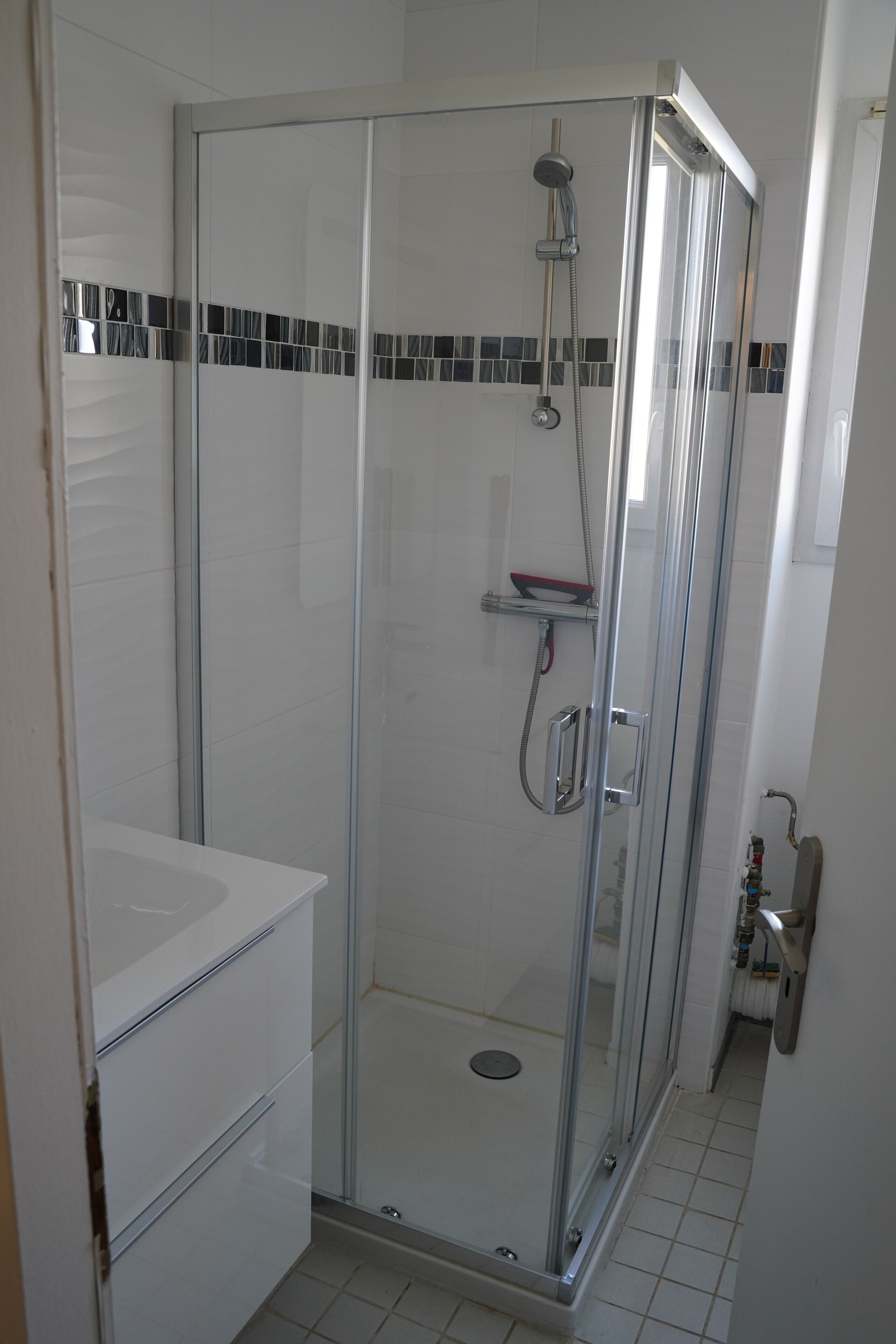 Een douchecabine met glazen wanden, een chroomdouchekop en een handdouche.