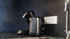 A modern kitchen with a stainless steel sink, a kettle, and a black countertop. - Apparts Confort 87 (Limoges)
