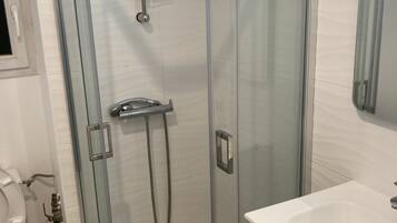 Een moderne badkamer met een douchecabine van glas, een witte wastafel en een toilet.
