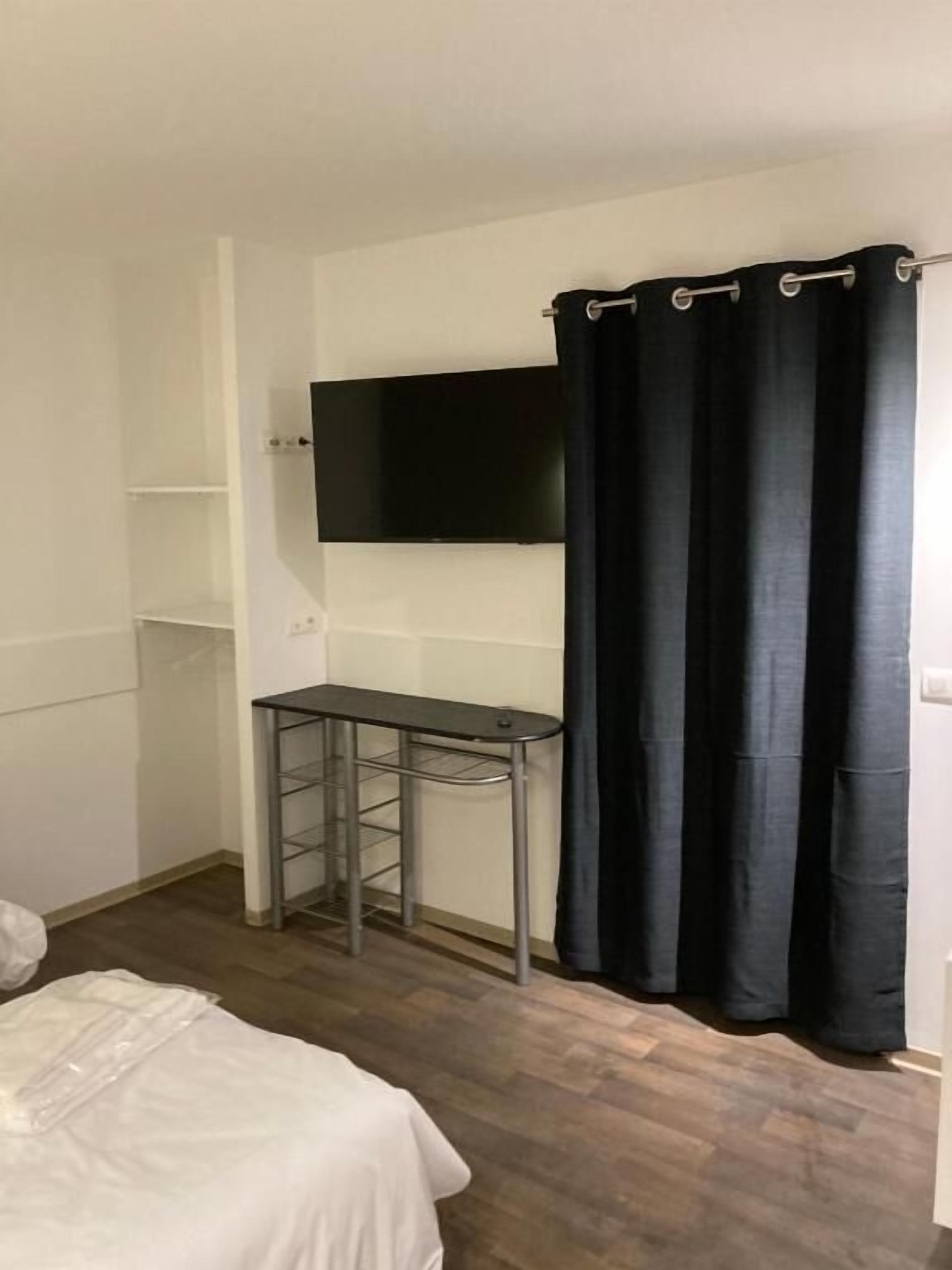 A small room with a bed, a desk, a TV mounted on the wall, and a black curtain.