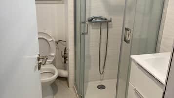 A bathroom with a glass-enclosed shower, a toilet, and a sink.