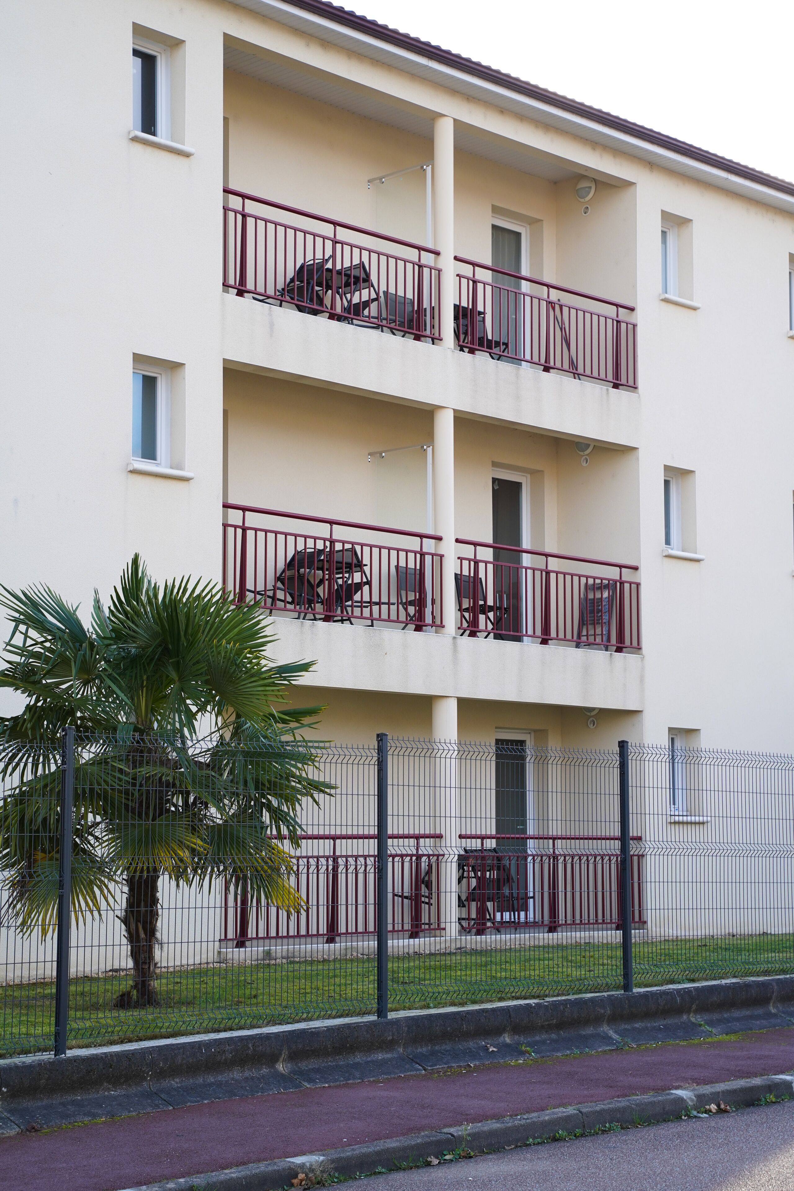 Un immeuble résidentiel à plusieurs étages, doté de balcons, d’un palmier et d’une clôture.
