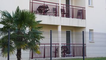 Un immeuble résidentiel à plusieurs étages, doté de balcons, d’un palmier et d’une clôture.