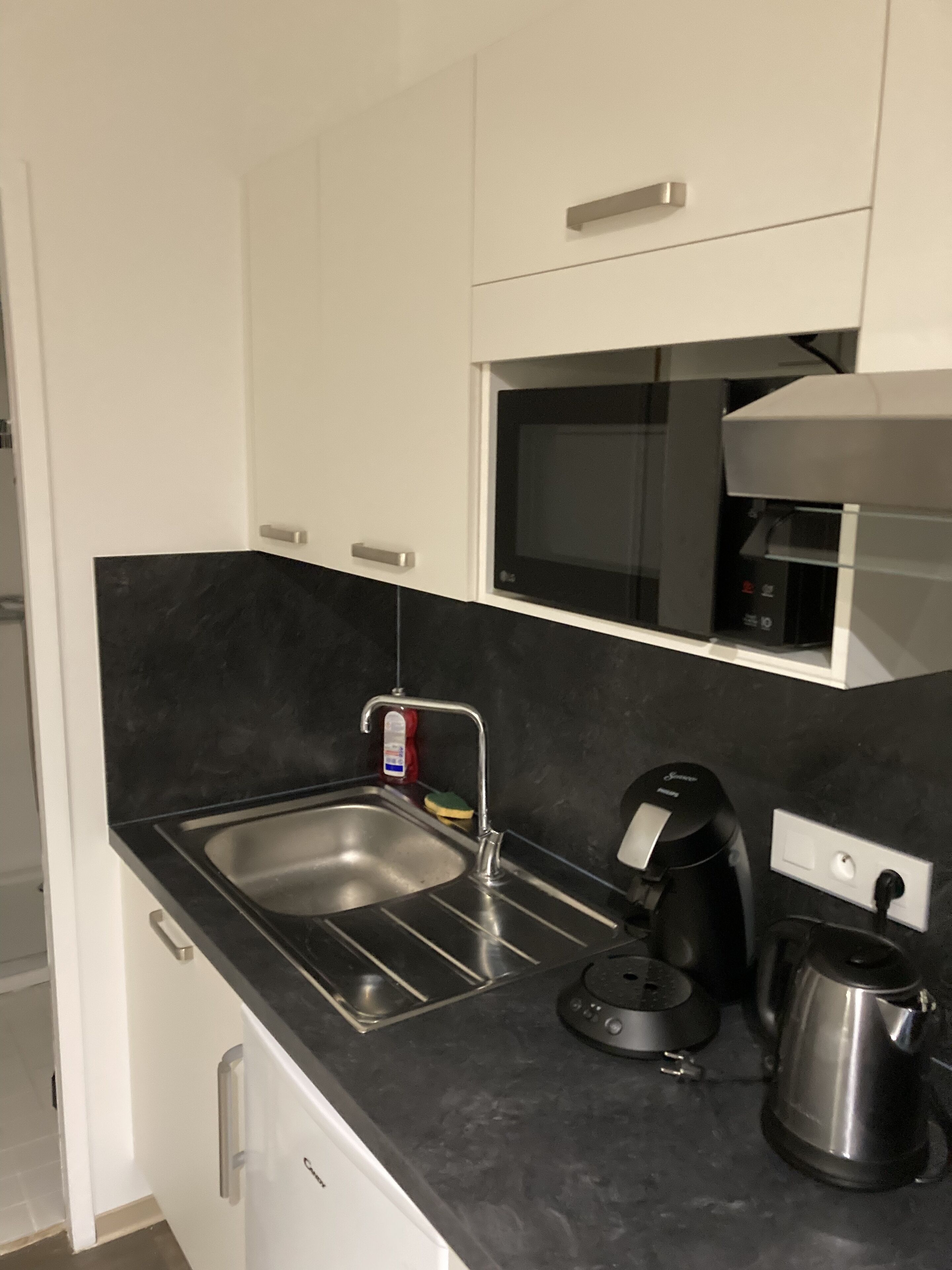 A modern kitchen with a black countertop, stainless steel sink, and a coffee maker.