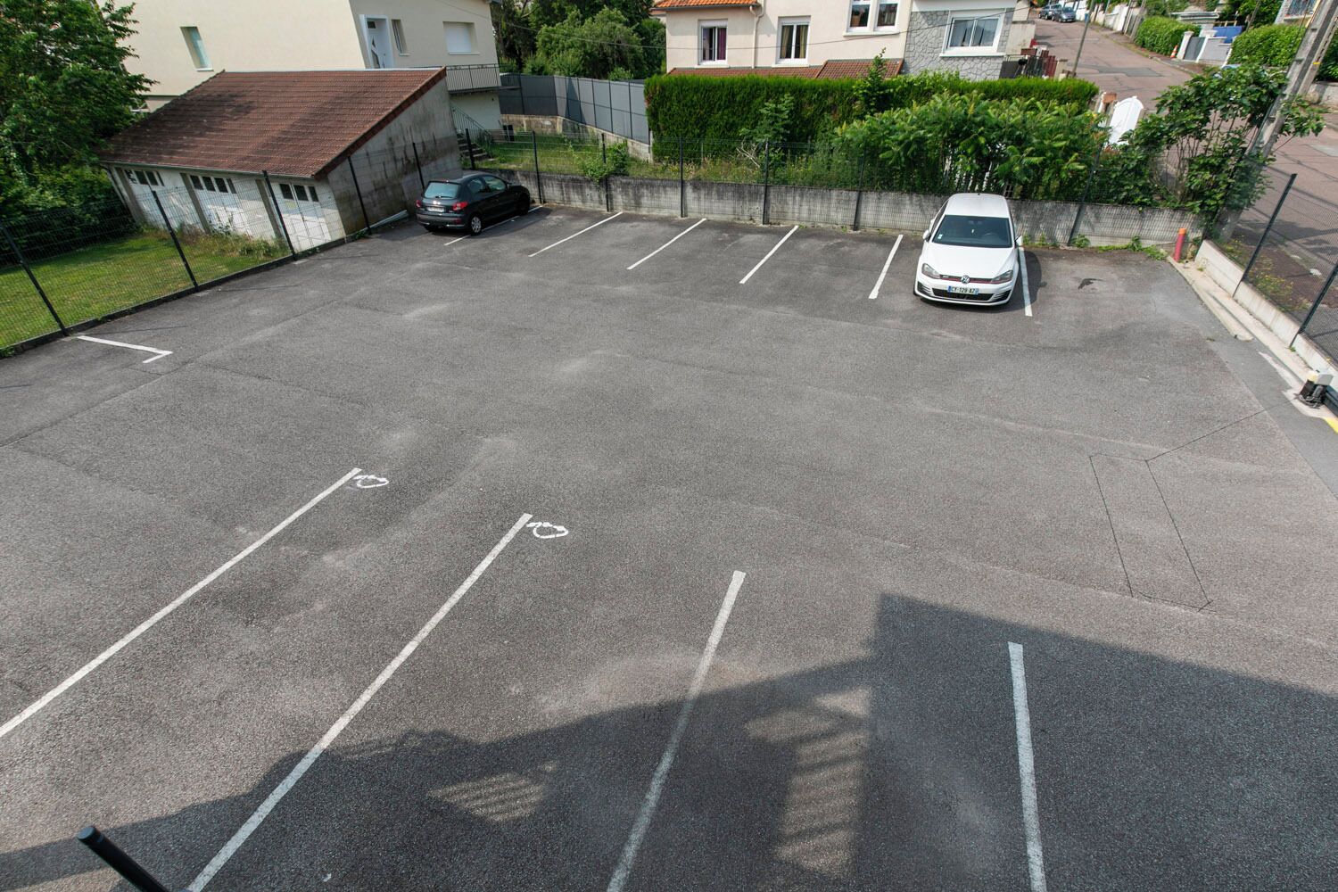 A parking lot with marked spaces, a white car, and a black car parked.