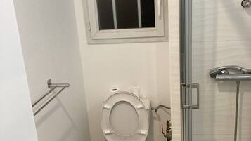 A bathroom with a toilet, a window, a shower, and a door.