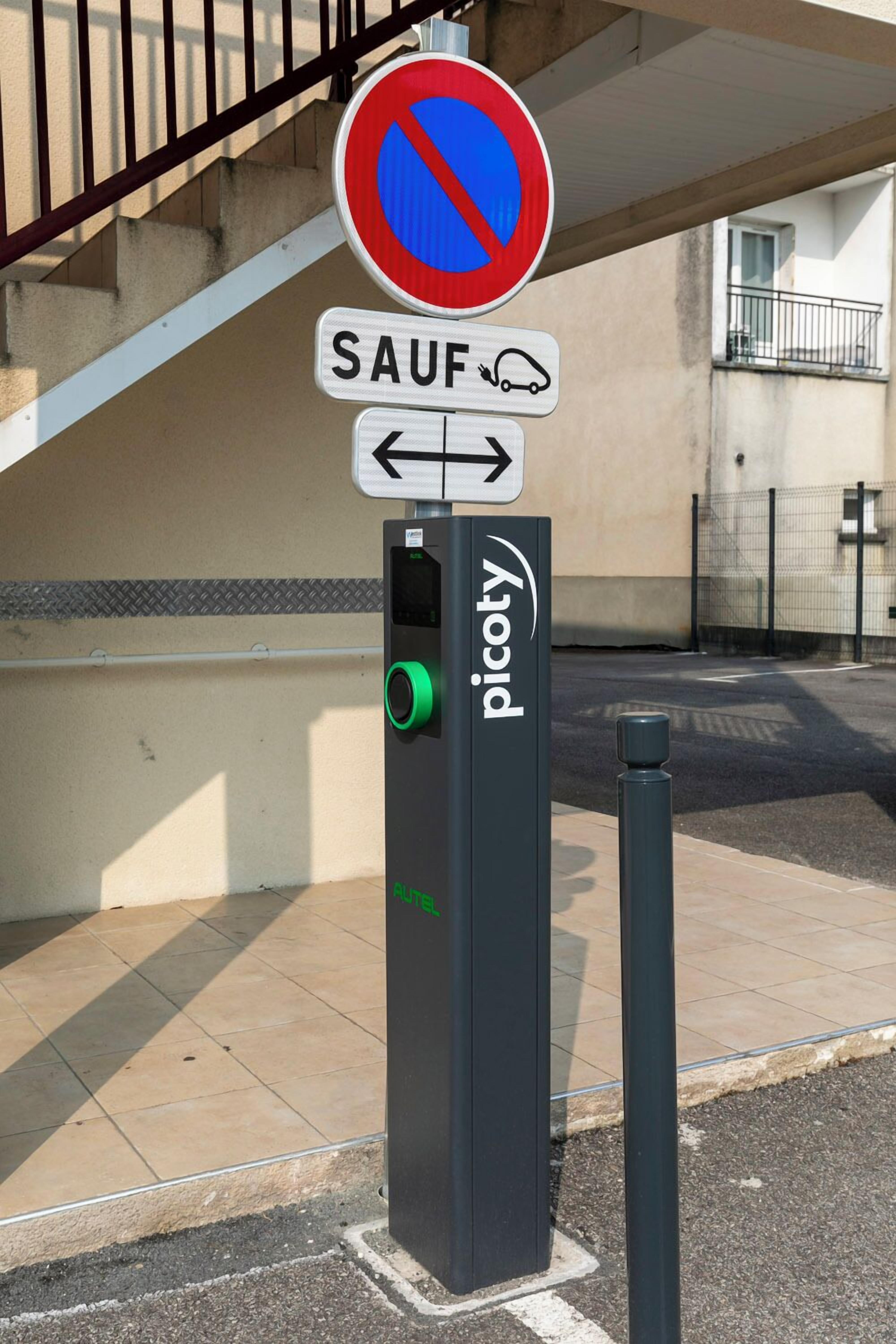 Un parcmètre surmonté d’un panneau indiquant l’interdiction de se garer, un panneau de signalisation et un bâtiment en arrière-plan.
