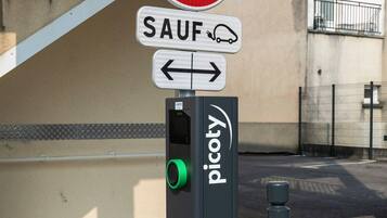 Un parcmètre surmonté d’un panneau indiquant l’interdiction de se garer, un panneau de signalisation et un bâtiment en arrière-plan.