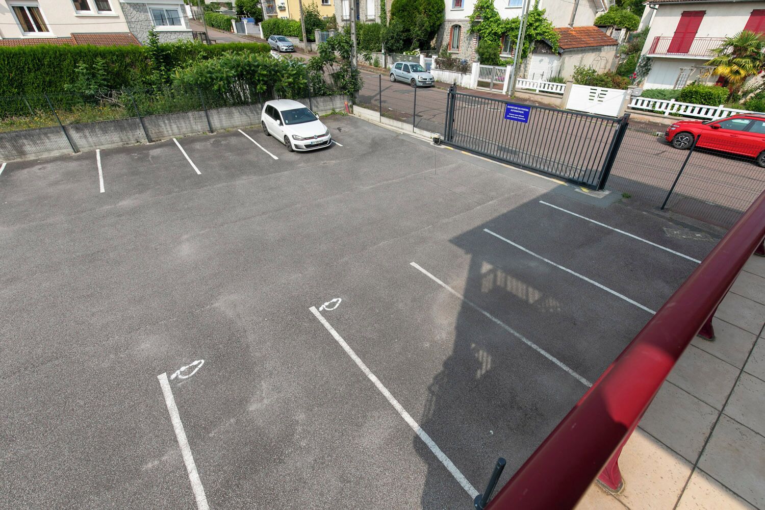 Een parkeerplaats met aangegeven parkeerplaatsen, een hek en een rode auto erin.
