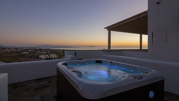 A hot tub on a balcony with a view of the sea and distant buildings. - Villa Bella, Mikri Vigla.  Private pool, jacuzzi & amazing views. Sleeps 10+. (Naxos)