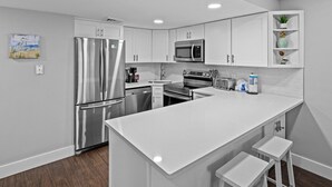 Une cuisine moderne avec des meubles blancs, des appareils en acier inoxydable et un îlot central doté de tabourets de bar.