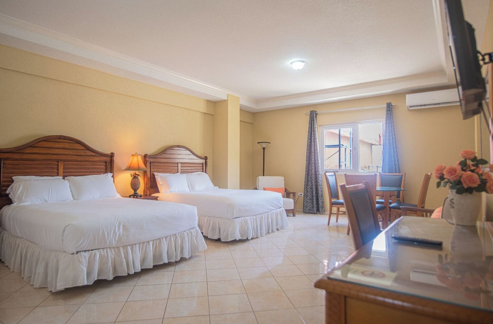 Habitación de hotel con dos camas, una zona de comedor y vistas al exterior.
