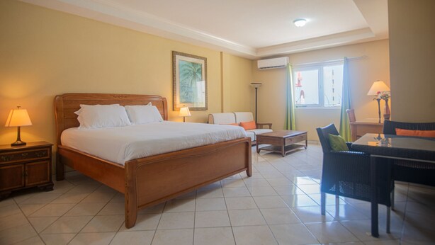 A hotel room with a wooden bed, a small table, a chair, and a desk. - NEW ! Bay Harbor studio 202 (Oranjestad)