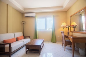 A furnished room with a sofa, a wooden table, a chair, a lamp, and a mirror.