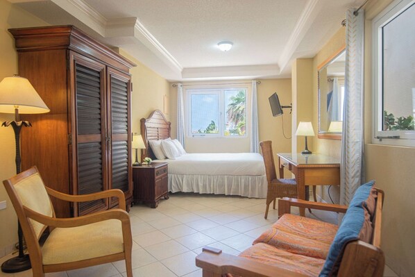 A hotel room with a bed, a desk, a chair, a wardrobe, and a window with a view of greenery.