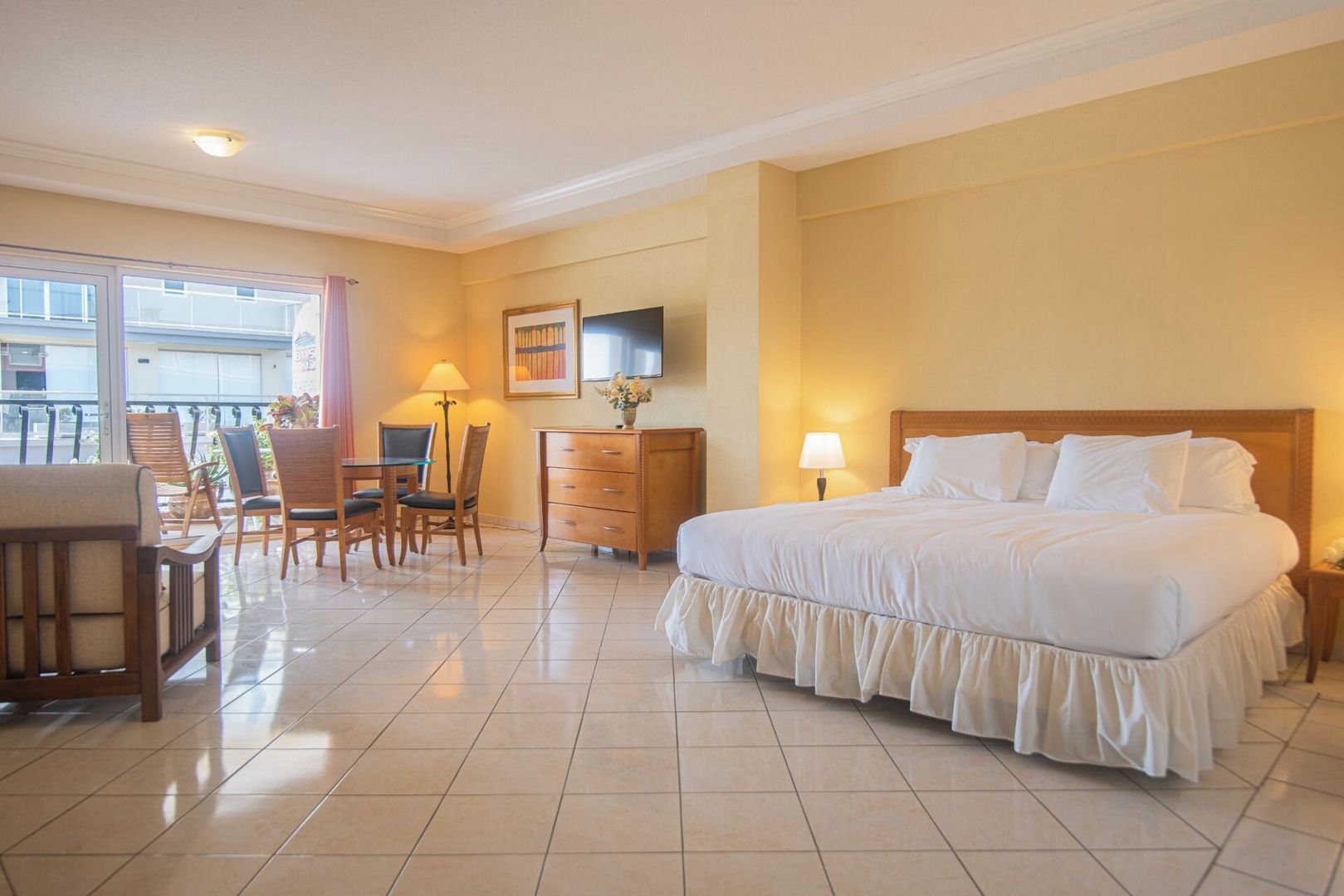 A hotel room with a bed, a desk, chairs, a dresser, and a TV on the wall.