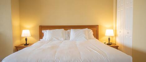 A neatly made bed with white linens, two bedside lamps, and a wooden headboard.