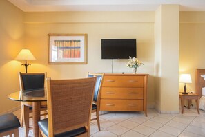 A hotel room with a dining table, chairs, a dresser, a television, and a lamp.