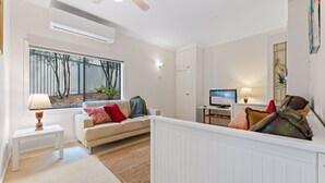 Ein modernes Wohnzimmer mit einem beigefarbenen Sofa, einem Fernseher und einem Fenster mit Blick auf Bäume.