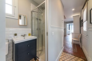 Ein modernes Badezimmer mit Duschkabine aus Glas, einem weißen Waschbecken mit dunklem Unterschrank und einem Schachbrettfußboden.