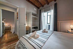 Ein Hotelzimmer mit einem großen Bett, einem Schrank, einem Schreibtisch mit Lampe und Blick durch ein Fenster nach draußen.