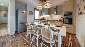 Une cuisine moderne avec un coin repas, comprenant un grand îlot central, des luminaires suspendus et des appareils électroménagers intégrés.