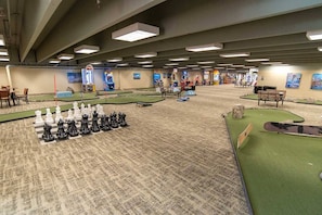 Un vaste espace intérieur comprenant un grand échiquier, plusieurs bornes d’arcade et une piste de bowling.