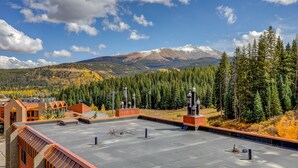 A rooftop terrace with a view of a snow-capped mountain, dense forest, and a clear sky.