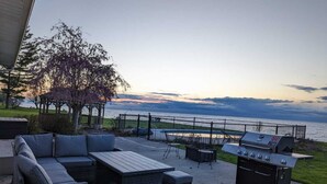 Une terrasse extérieure aménagée avec des meubles en osier, un barbecue et une vue sur l’eau.